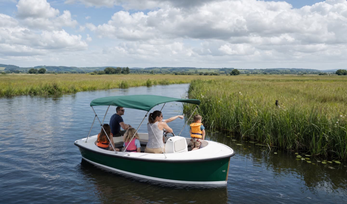 A woman aboard The Lapwing pointing out something in the reed bank while a small child in a lifejacket follows her hand